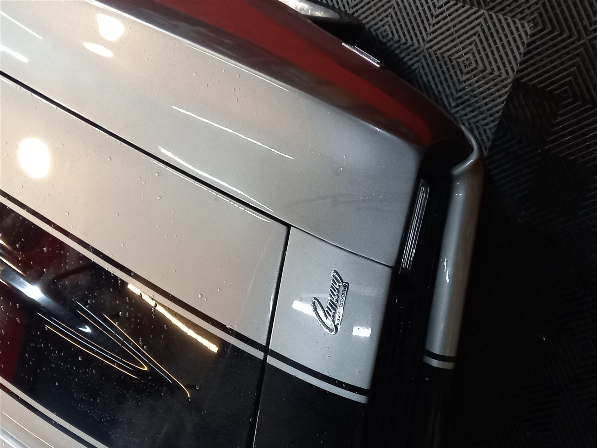Insignia 'Camaro by Chevrolet' sobre panel bicolor con gotas de agua, tras el sellado de la pintura.