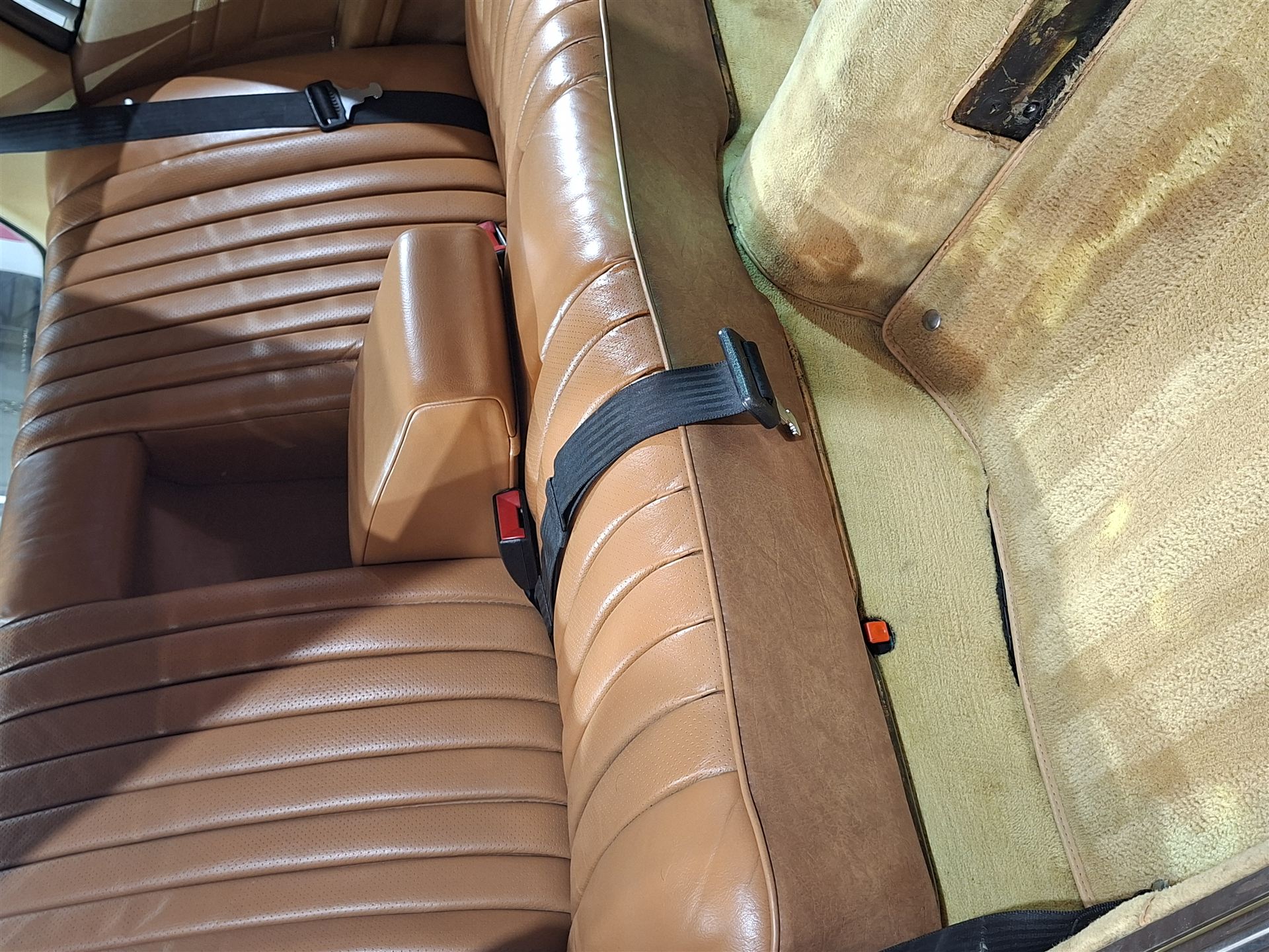 Asiento trasero de cuero color caramelo de un auto clásico, recién detallado, con cinturón de seguridad de época.