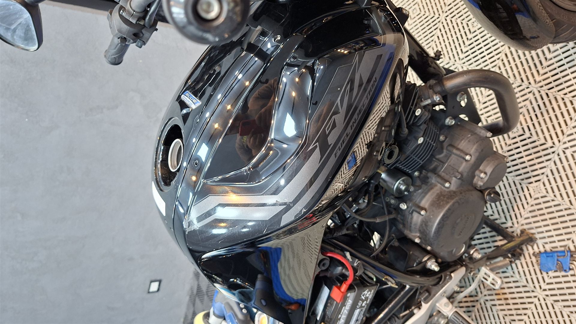 Tanque de combustible de una moto con inyección electrónica, terminación negra de alto brillo junto al motor.
