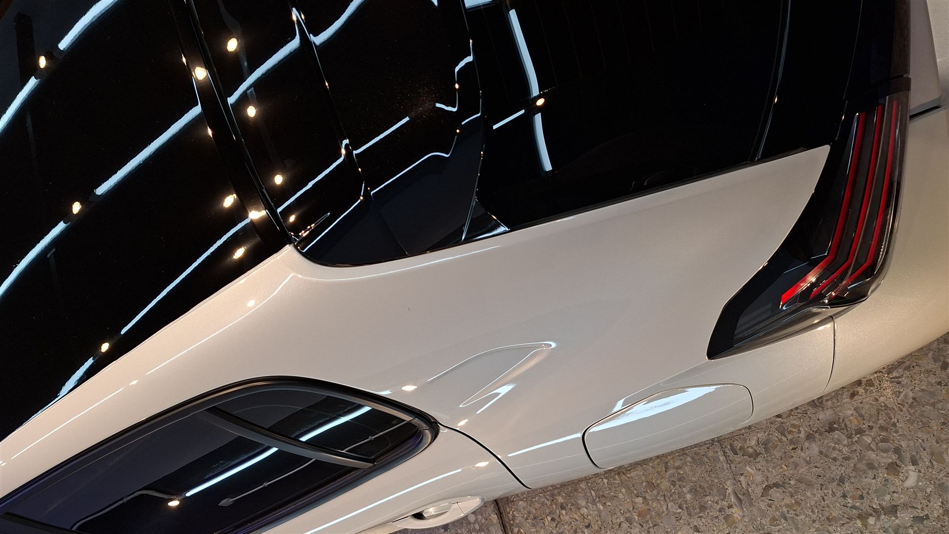 Panel trasero de un vehículo eléctrico blanco y negro con acabado espejado, reflejando las luces del taller.