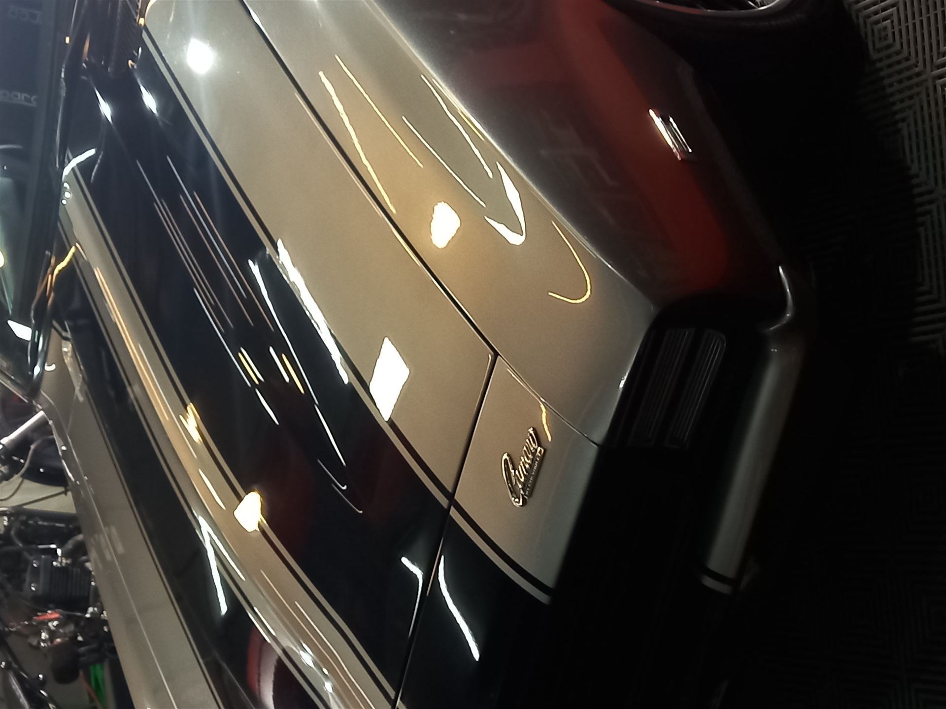 Panel lateral de un Chevrolet Camaro con brillo extremo tras el pulido de pintura, reflejando las luces del taller.